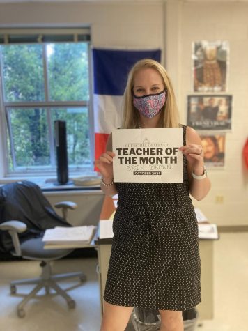 Erin Brown, an AP World and European History teacher, poses with her Teacher of the Month sign in front of her French flag and historical memes. Her walls are decorated with the flags of different countries in Europe and around the world.