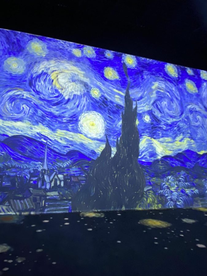 The Van Gogh Exhibition: the Immersive Experience surrounds viewers in artwork. The room is covered corner to corner with the famous painting, The Starry Night.
