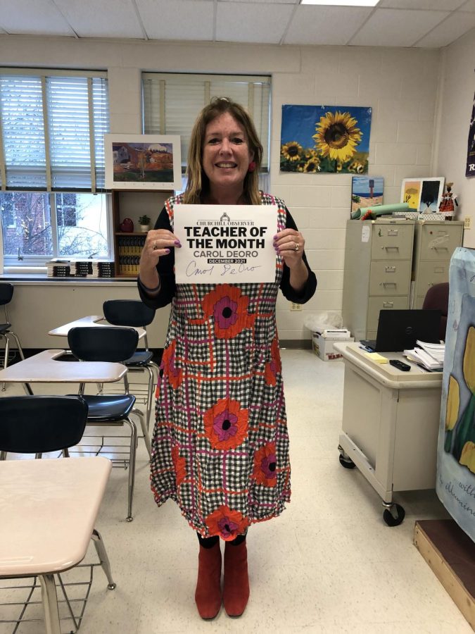 Carol DeOro, an Honors English 12 and AP Language and Composition teacher, holds up her Teacher of the Month sign in her classroom. DeOro has been teaching English for 31 years and loves helping her students improve their reading and writing skills.