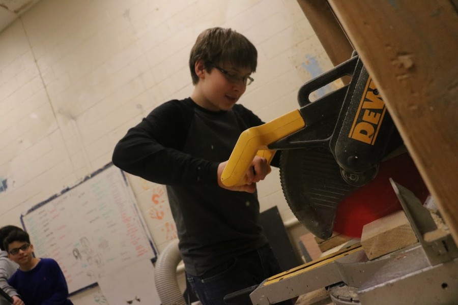 Freshman Ethan Finke uses tech power tools to cut a piece of wood that will help finish the set design.  