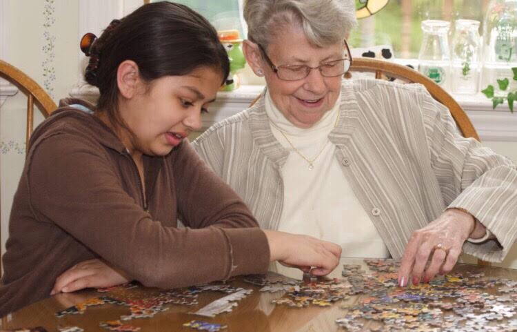 A+child+helps+an+elderly+woman+in+an+assisted+living+home+with+a+puzzle.
