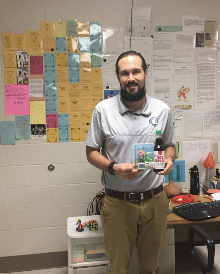 Mr. Antonucci stands in his office holding his gift of a Peppa Pig and the soysauce while he is surrounded by the written cards all over the walls. 