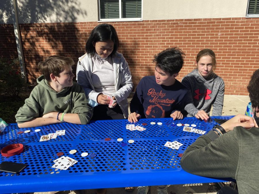 Sophomore Zoey Tahardi (standing in the blue jacket) deals the cards out for blackjack at lunch on Oct. 28. She plays blackjack with her group of friends near-daily at lunch, often in the courtyard next to the math department.