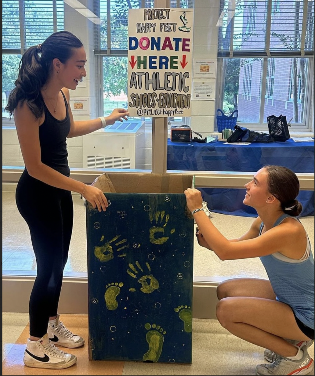 WCHS students Laura Jablonover (left) and Kaylee Tasin (right) stand next to the Project Happy Feet donation box in WCHS. This donation box is near the main office and accepts shoes along with other sports equipment. 