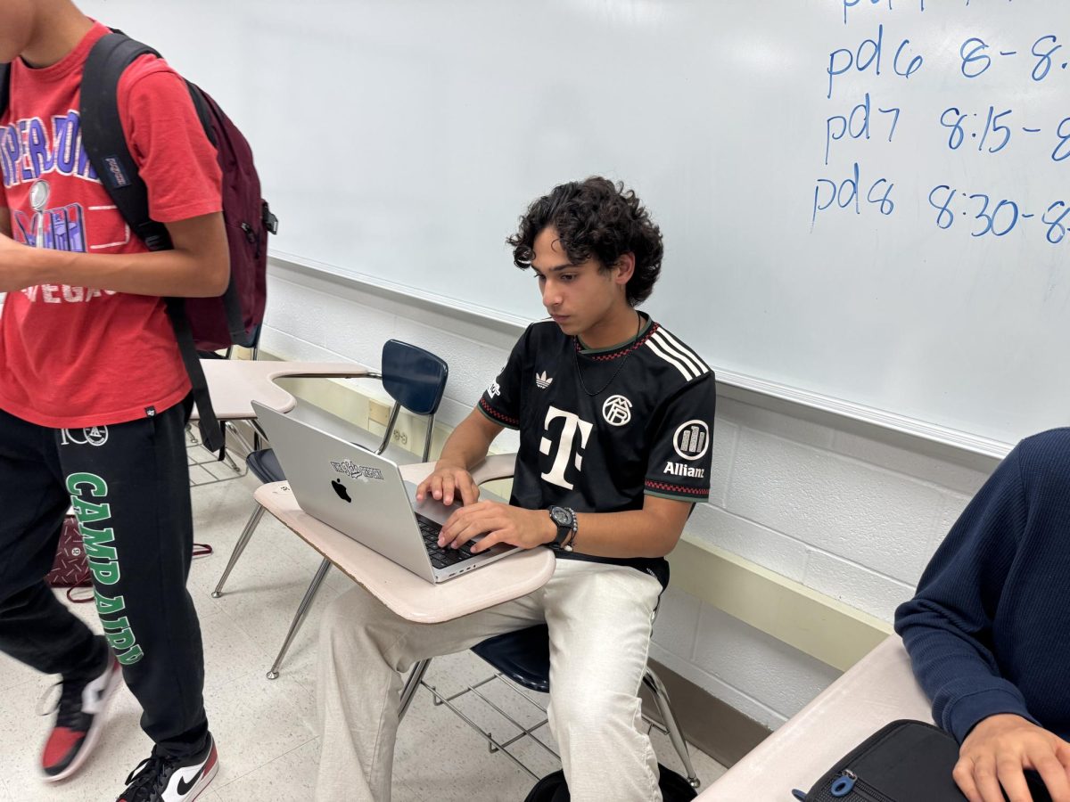 A WCHS freshman uses a MacBook Pro before class, finishing his work that could not be completed on a chromebook before the bell rings. The new policy would require him to put the device away when class starts.